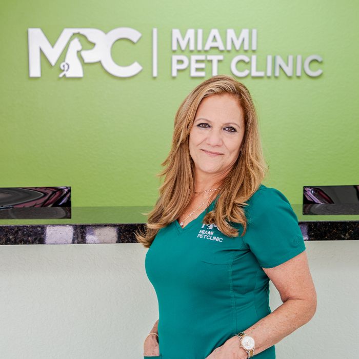 Woman in teal scrubs standing at a reception desk at Miami Pet Clinic.